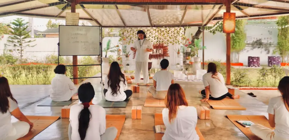Teacher Ian guiding a seated class dressed in white in the open-air pavilion, with a whiteboard beside him